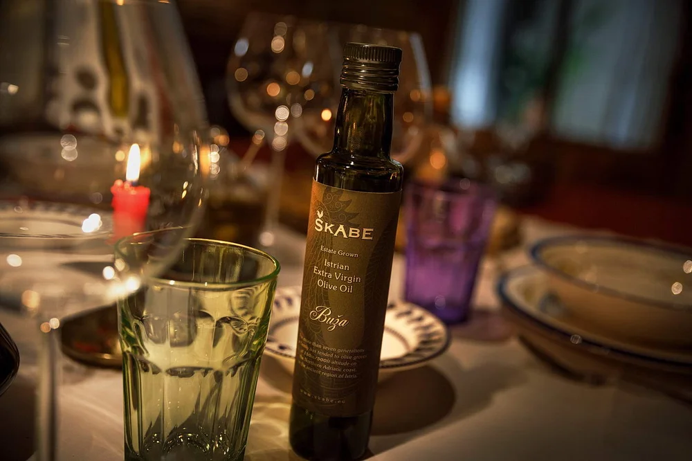 Dark glass bottle of Škabe Estate Grown Istrian Extra Virgin Olive Oil Buža on a dining table
