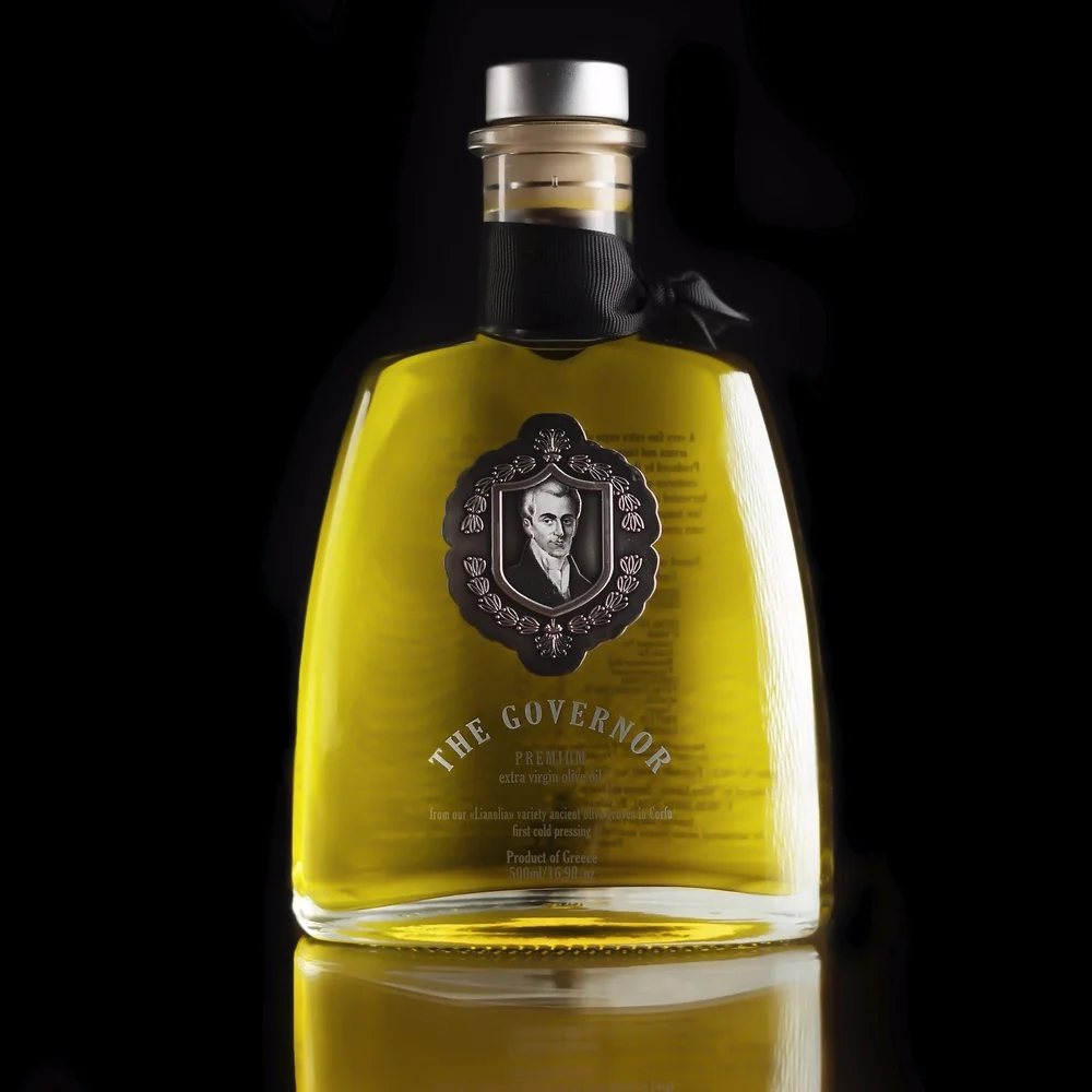 Clear glass bottle of The Governor Premium Edition extra virgin olive oil with a silver portrait medallion and black neck ribbon